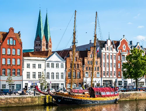Historische Gebäude in der Lübecker Altstadt an der Trave. Im Vordergrund ist ein altes Segelboot. Foto: FooTToo, iStock.com