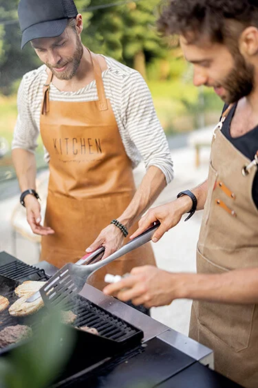 Ausschnitt eines Grills mit Fleisch, an dem zwei Männer stehen. Foto: RossHellen, istock.com