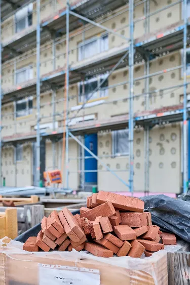 Foto des Rohbaus und den zugeschmierten Löchern für die Elektroinstallation im Hintergrund. Im Vordergrund sind die roten Ziegel für die Fassade auf einem Haufen zu sehen..