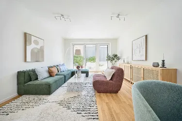 Wohnzimmer des Musterhauses von UP TOWN Houses. Blick auf die Sofalandschaft und durch die Fenster in den Garten.
